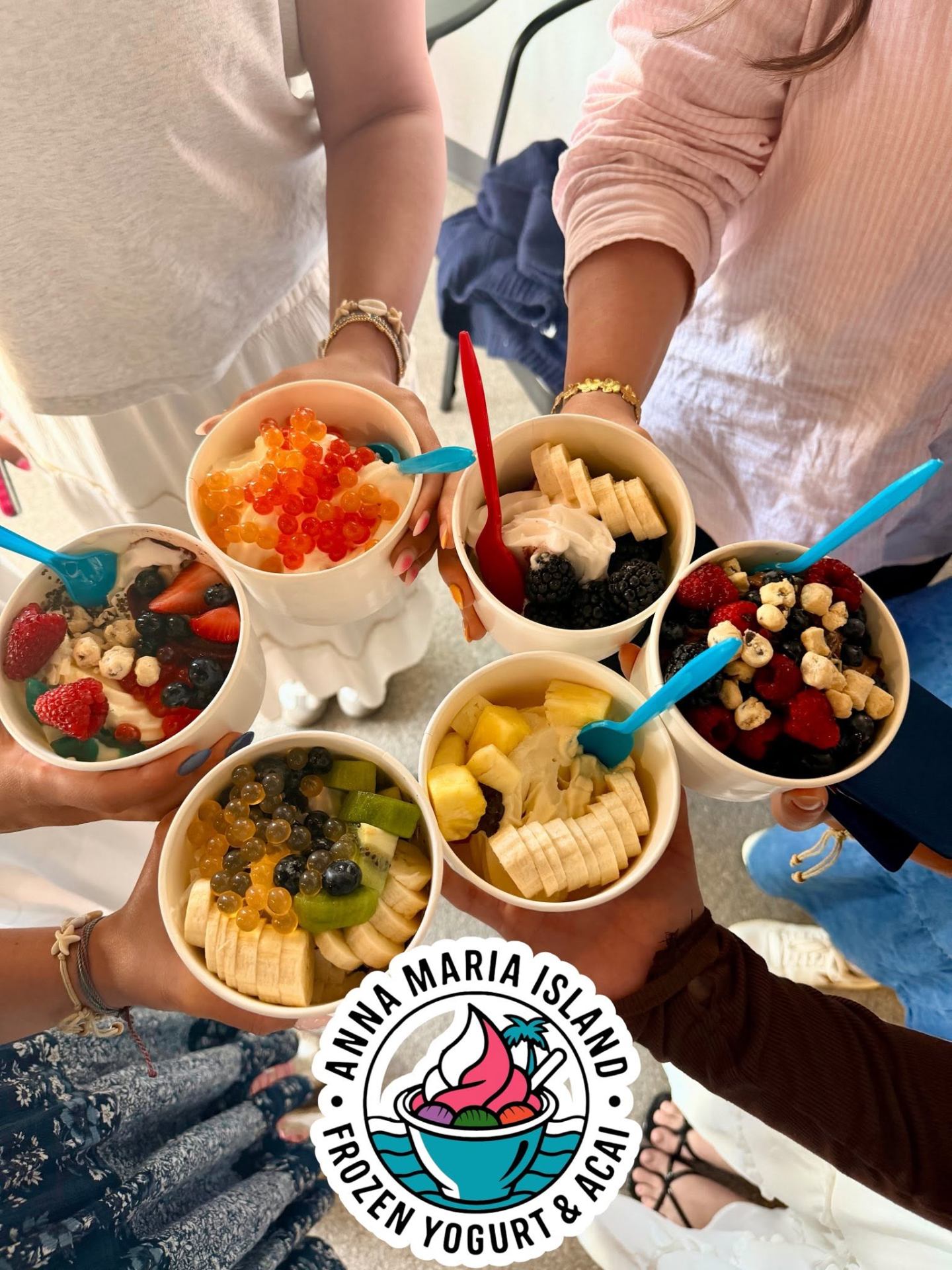 Six colorful frozen yogurt cups with popping boba, berries and fruit held in a circle